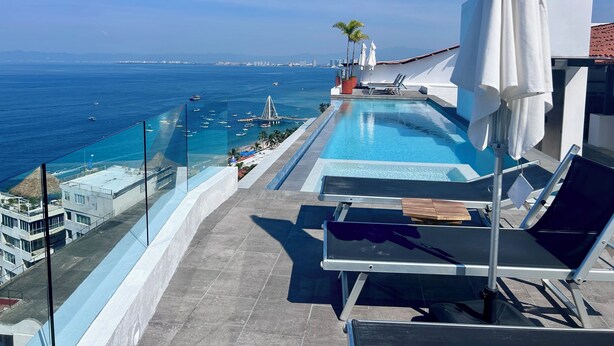 A rooftop infinity pool with a view of the sea and city skyline.