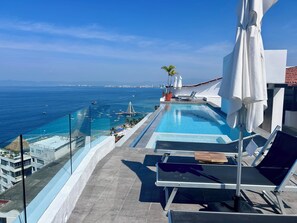 A rooftop infinity pool with a view of the sea and city skyline.