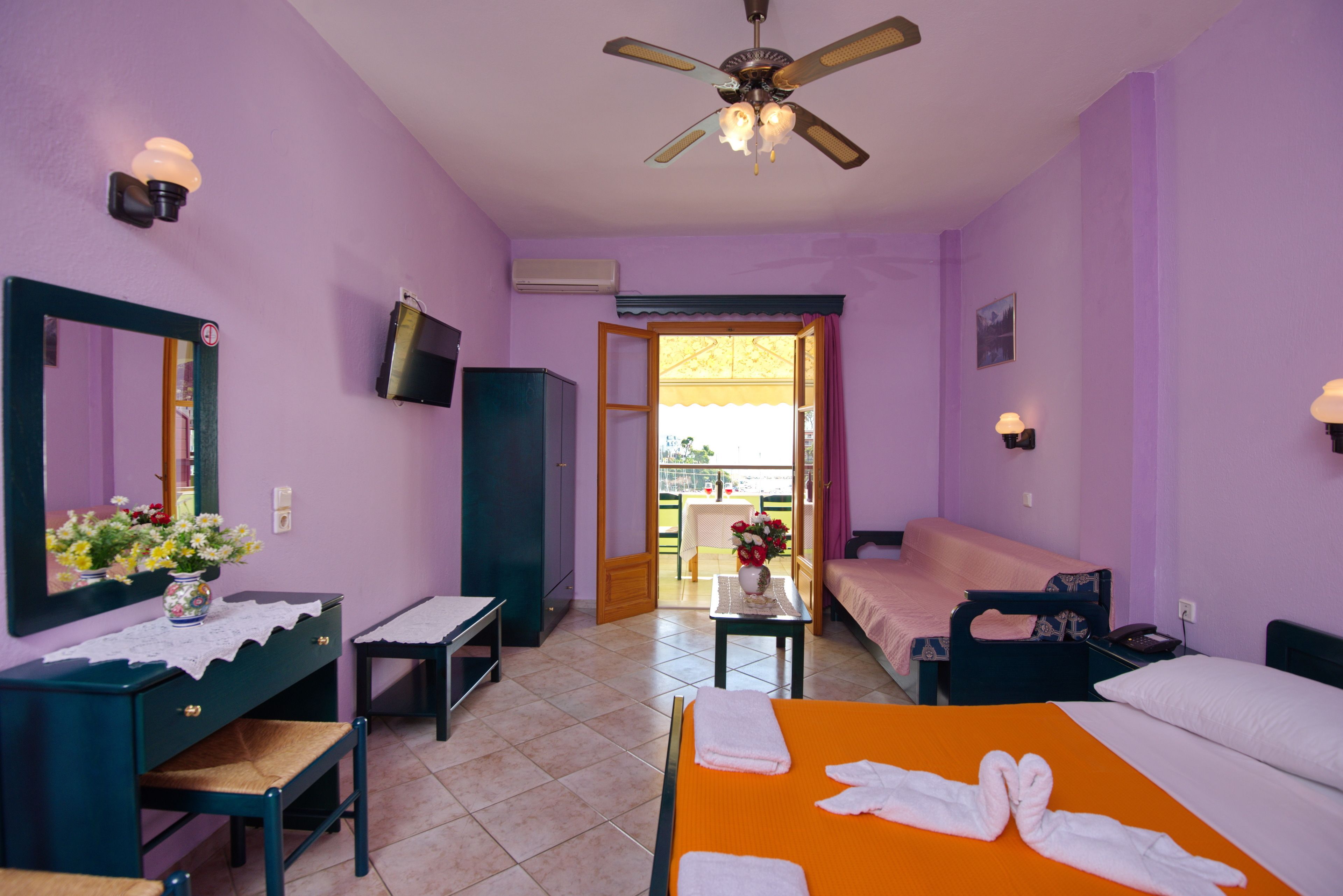 A hotel room with a bed, a desk, a chair, a TV, and a balcony with a table and chairs.