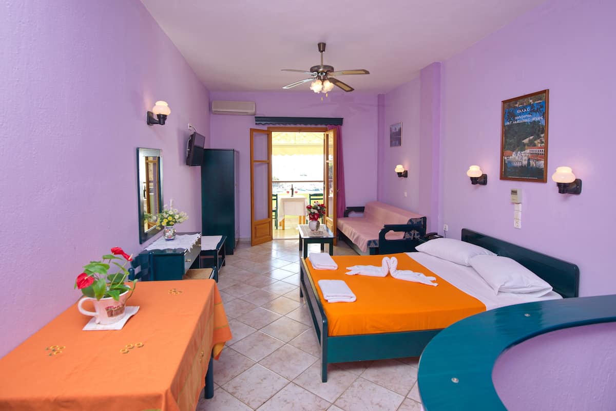 A hotel room with two beds, a table with a vase of flowers, a ceiling fan, and a view of the outside.