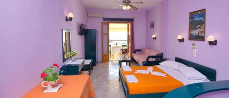 A hotel room with two beds, a table with a vase of flowers, a ceiling fan, and a view of the outside.