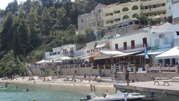 A coastal town with a beach, buildings, and a dock with boats. - Haravgi Hotel (Alonissos)