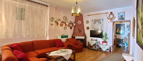 Un salon avec un canapé rouge, une table basse en bois et une cheminée. Des assiettes décoratives ornent le mur et un téléviseur est fixé au-dessus de la cheminée.