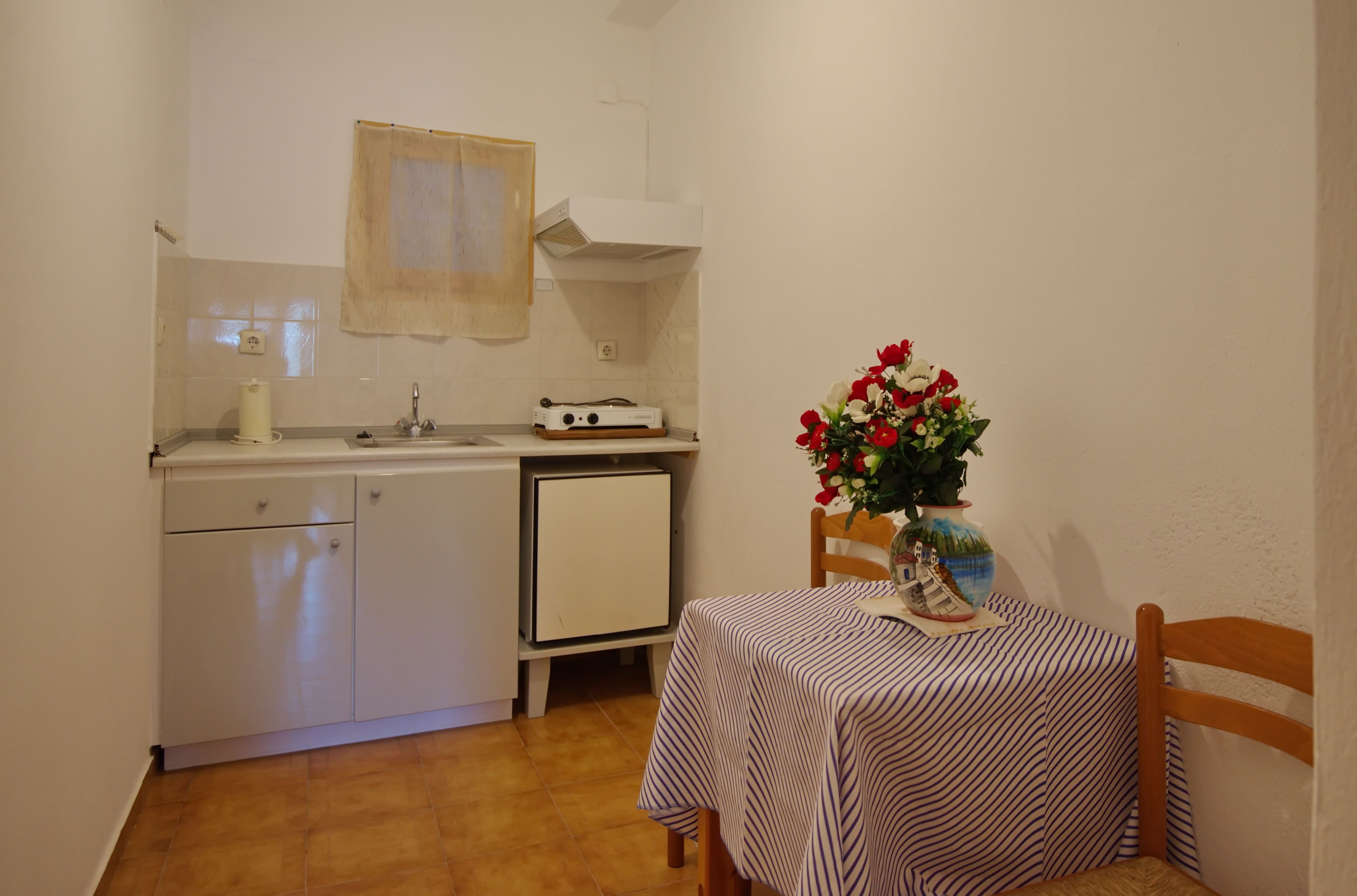 A compact kitchen with a small island, a dining table with a striped tablecloth, and a potted plant with flowers.
