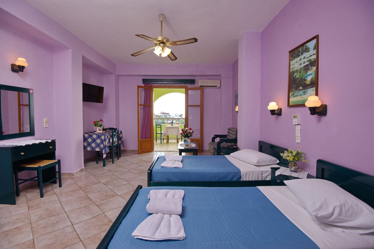 A hotel room with two beds, a desk, a chair, a table, and a balcony with a view.