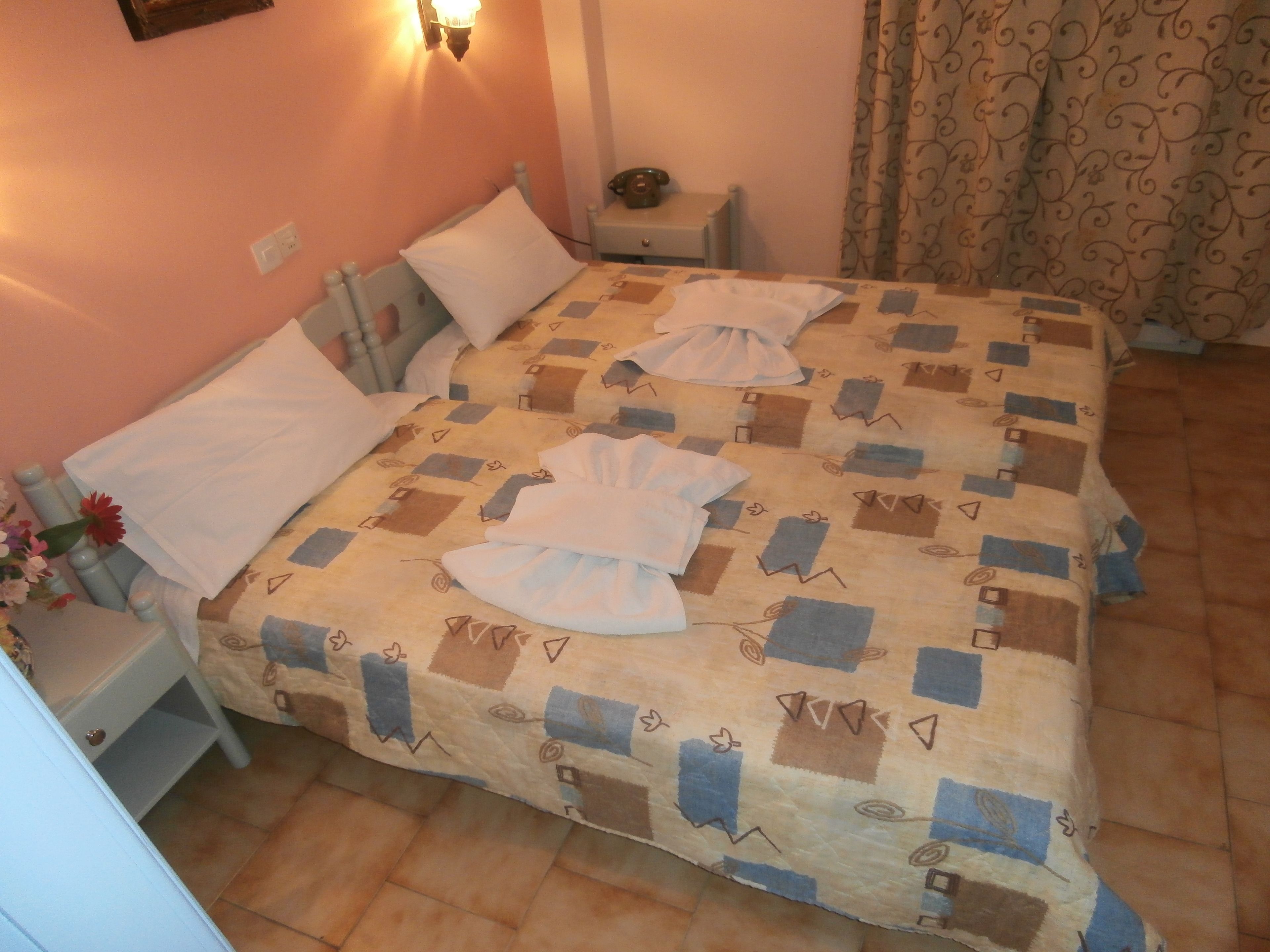 A neatly made bed with a patterned bedspread, a bedside table with a lamp, and a small nightstand with a telephone.