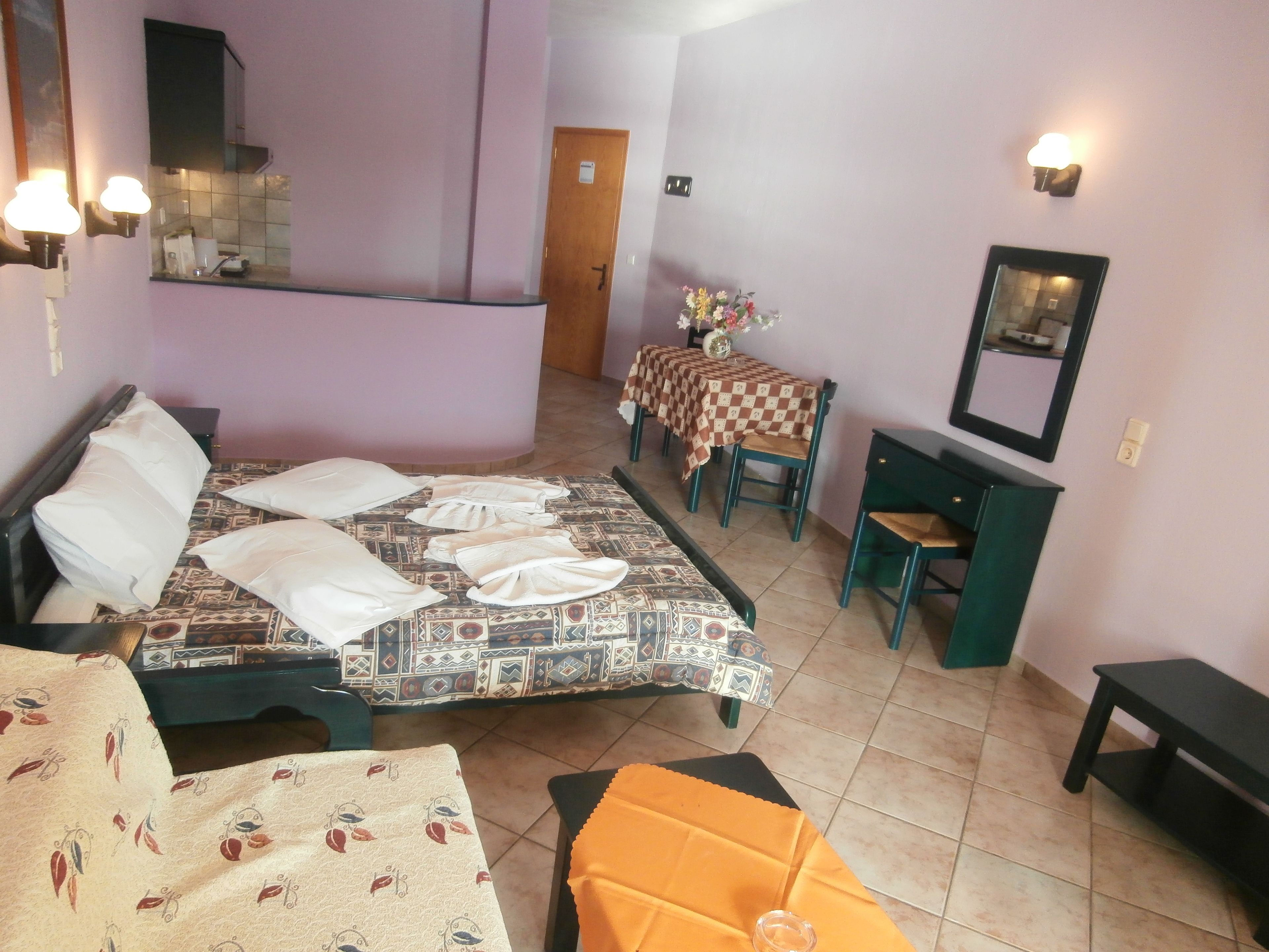 Una habitación de hotel con cama, escritorio, silla, una pequeña mesa con mantel a cuadros y un espejo en la pared.
