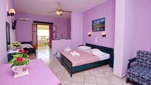 A room with a bed, a chair, a table with a vase of flowers, and a painting on the wall. - Haravgi Hotel (Alonissos)