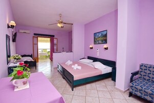 Una habitación con una cama, una silla, una mesa con un jarrón de flores y un cuadro en la pared.
