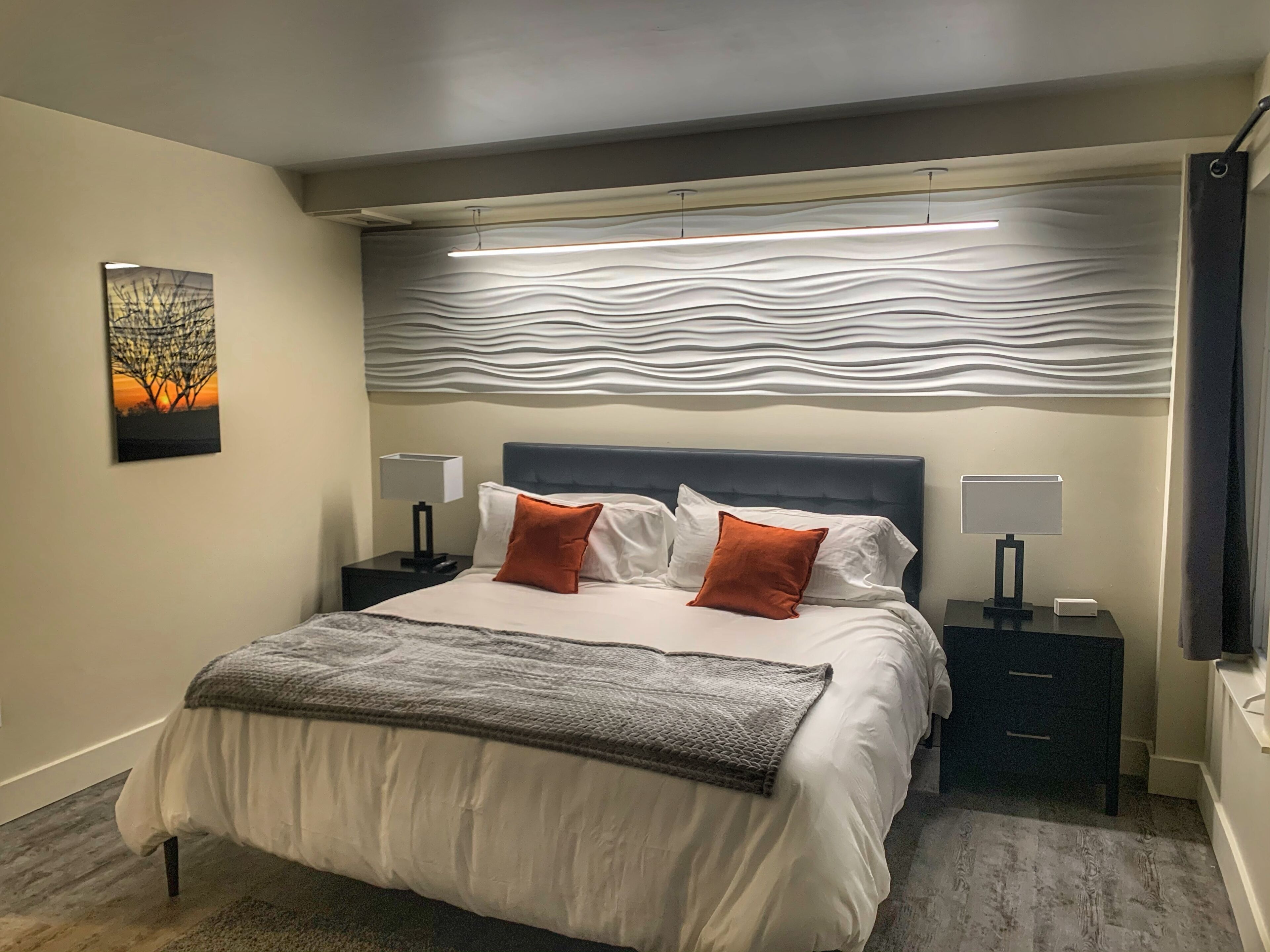 Une chambre moderne avec un grand lit, deux tables de chevet, une lampe fixée au mur et un panneau décoratif mural.