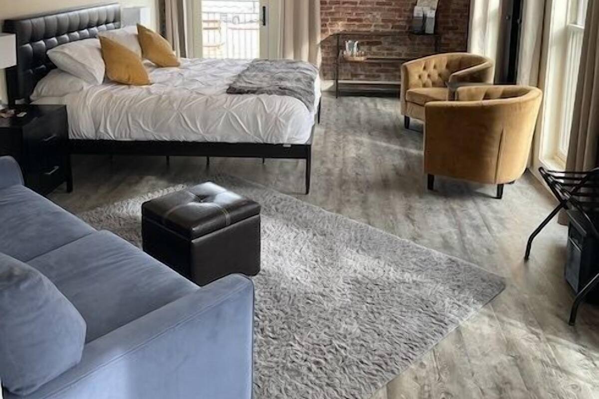 Un dormitorio moderno con pared de ladrillo, una cama, un sofá, un televisor y una chimenea.