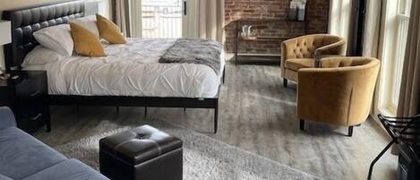 A modern bedroom with a brick wall, a bed, a sofa, a TV, and a fireplace.