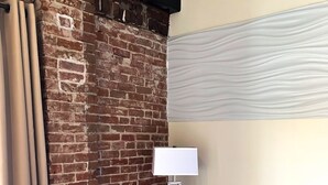 Een kamer met twee blauwe fauteuils, een bakstenen muur, een witte lamp en een raam met een witte gordijn.