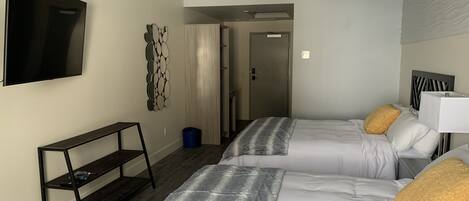 Ein Hotelzimmer mit zwei Betten, einem Fernseher, einem Regal und einer Tür zu einem Badezimmer.