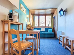 A cozy room with a wooden table, a blue sofa, and a television mounted on the wall. - Arcelle 216 by Interhome (Val Thorens)