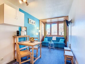 A compact living space with a kitchenette, a dining area, a sofa, and a window with a view of buildings. - Arcelle 216 by Interhome (Val Thorens)
