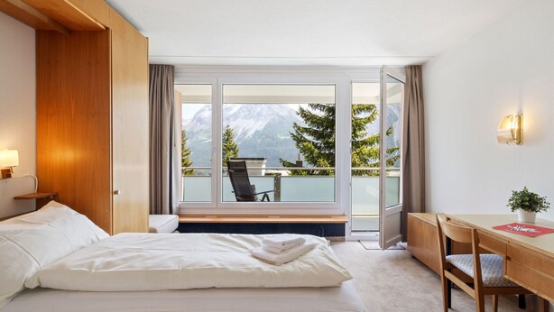 Ein Hotelzimmer mit Bett, Schreibtisch und Bergblick durch große Fenster.
