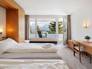 A hotel room with a bed, a desk, and a view of mountains through large windows.