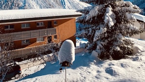 Eine verschneite Berglandschaft mit einem Gebäude, das einen Balkon hat, und einem verschneiten Baum im Vordergrund.