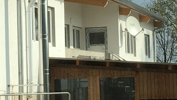 Un edificio de fachada blanca, con ventanas visibles y una antena parabólica en el techo.