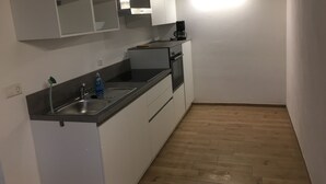 Una cocina compacta con armarios blancos, un lavamanos de acero inoxidable y piso de madera.