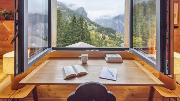 A wooden cabin with a large window offering a view of a mountainous landscape.