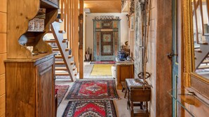 A wooden interior with a staircase, a traditional cabinet, and a patterned rug.