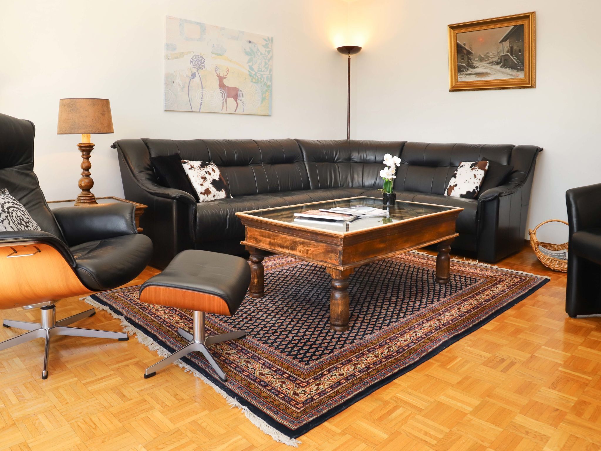 A living room with a black leather sofa, a glass coffee table, a patterned rug, and a lamp.