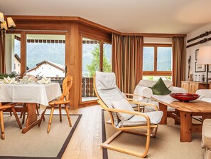 Un intérieur en bois comprenant une table à manger pour quatre personnes, un canapé et un fauteuil offrant une vue sur les montagnes.