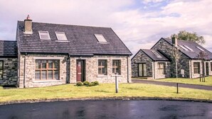 A row of stone houses with pitched roofs and skylights, a grassy area in front, and a paved driveway.