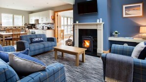 A modern living room with a fireplace, blue sofas, and a kitchen in the background.