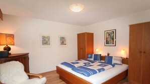 Un dormitorio con una cama de madera, una silla blanca, un armario de madera y un escritorio con una lámpara.