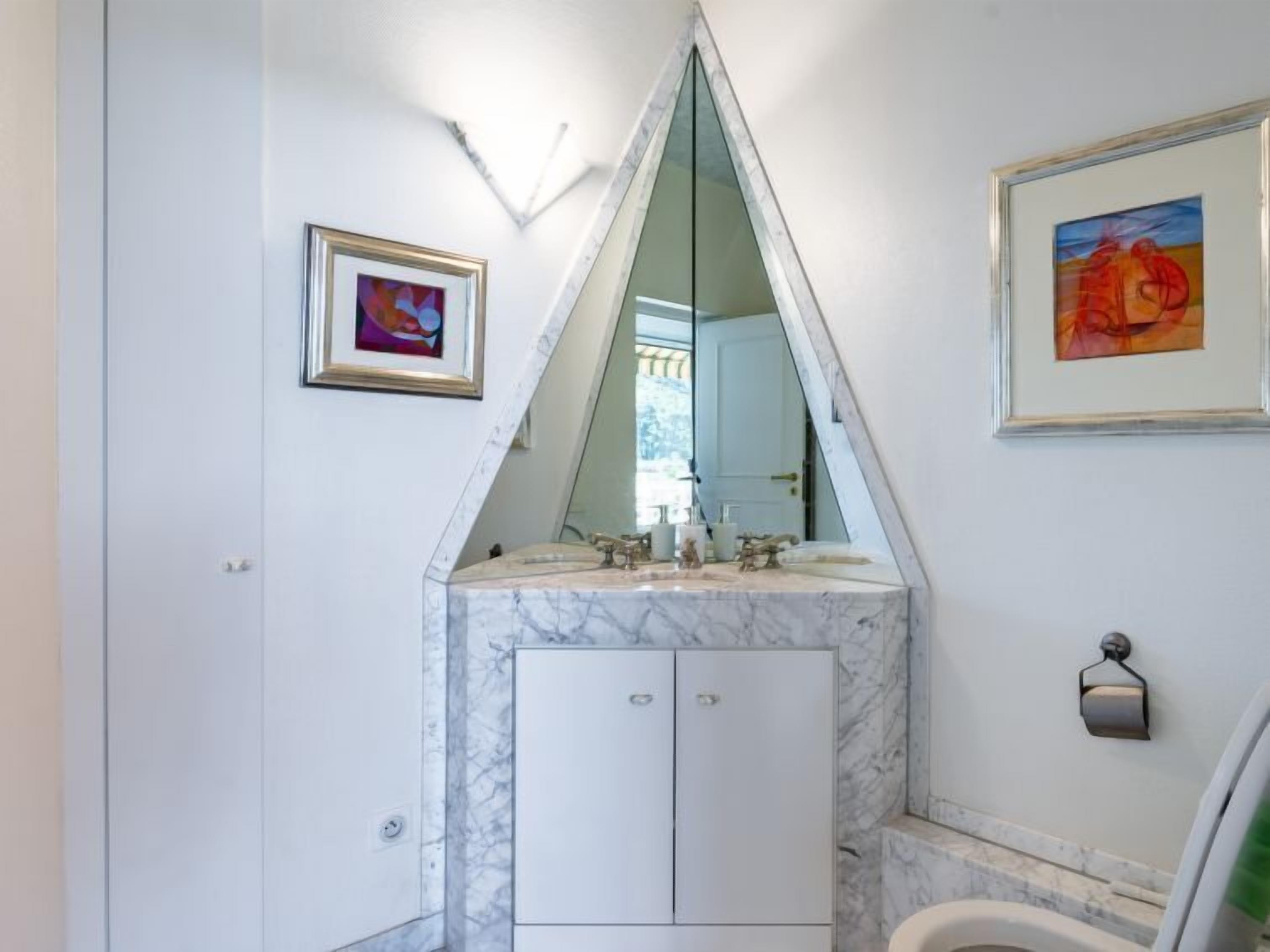 A bathroom with a marble vanity, a large mirror, and two framed artworks on the walls.