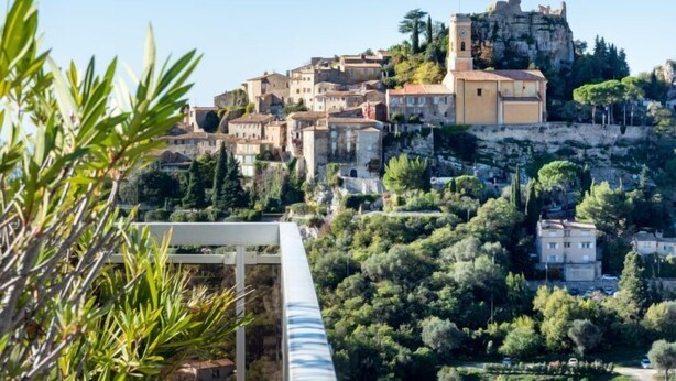 Une ville pittoresque, située sur une colline, avec des bâtiments historiques, une tour imposante et une végétation luxuriante.