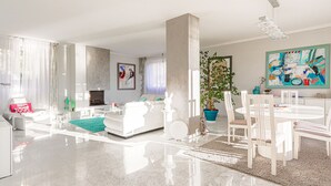 Un salon spacieux avec un canapé blanc, une table à manger avec des chaises, une cheminée et un grand tableau abstrait.