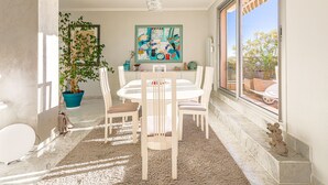 Un coin repas avec une table ronde, des chaises blanches, une plante en pot et un tableau abstrait aux couleurs vives accroché au mur.