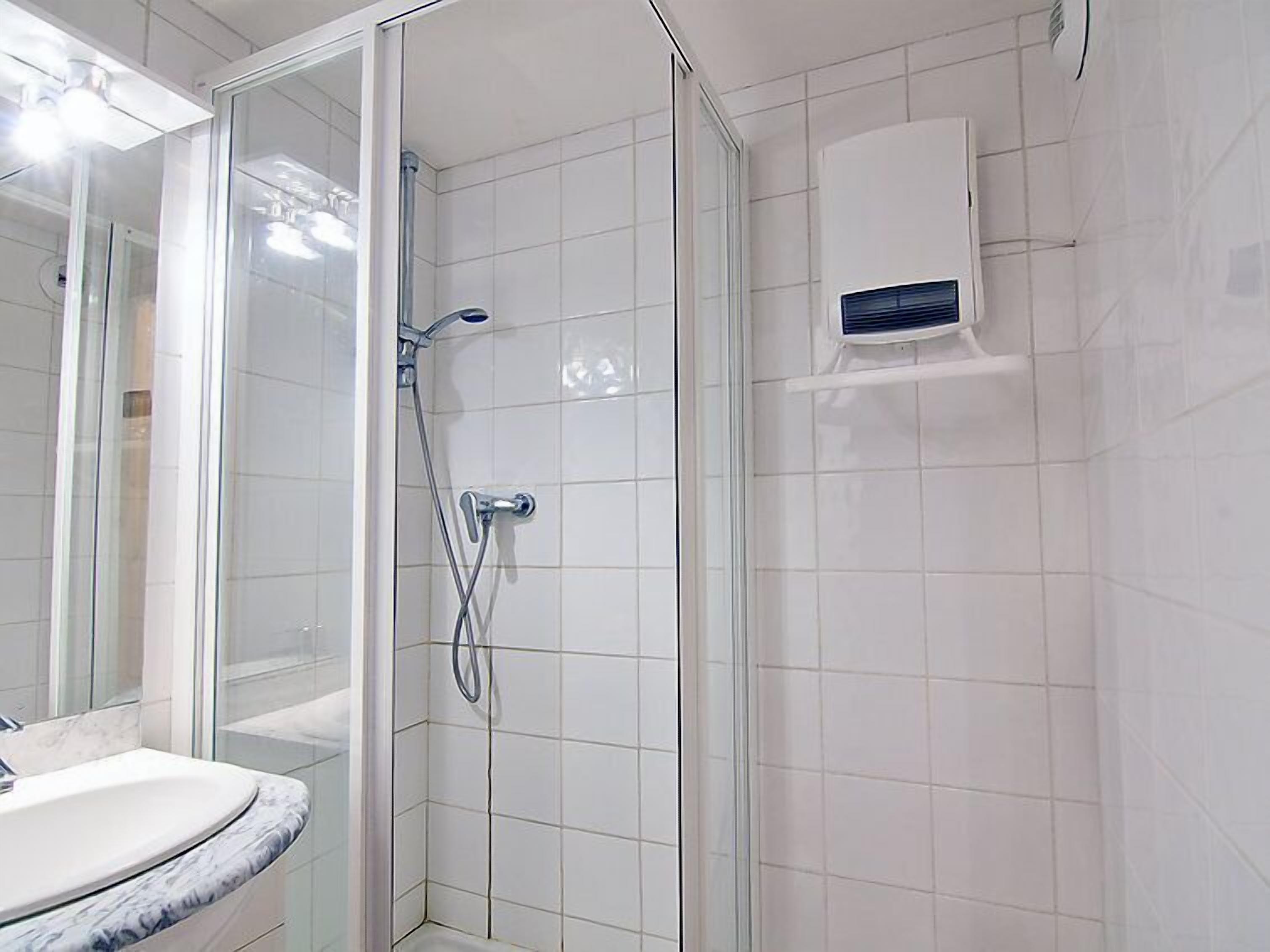 A modern bathroom with a glass shower enclosure, a white tiled wall, and a built-in ventilation unit.