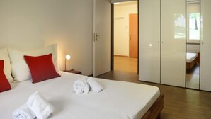 A modern hotel room with a large bed, red pillows, white towels, a bedside lamp, and a wardrobe.