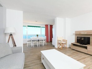 Una sala de estar moderna con un sofá blanco, un mueble para televisión y un comedor con mesa y sillas.