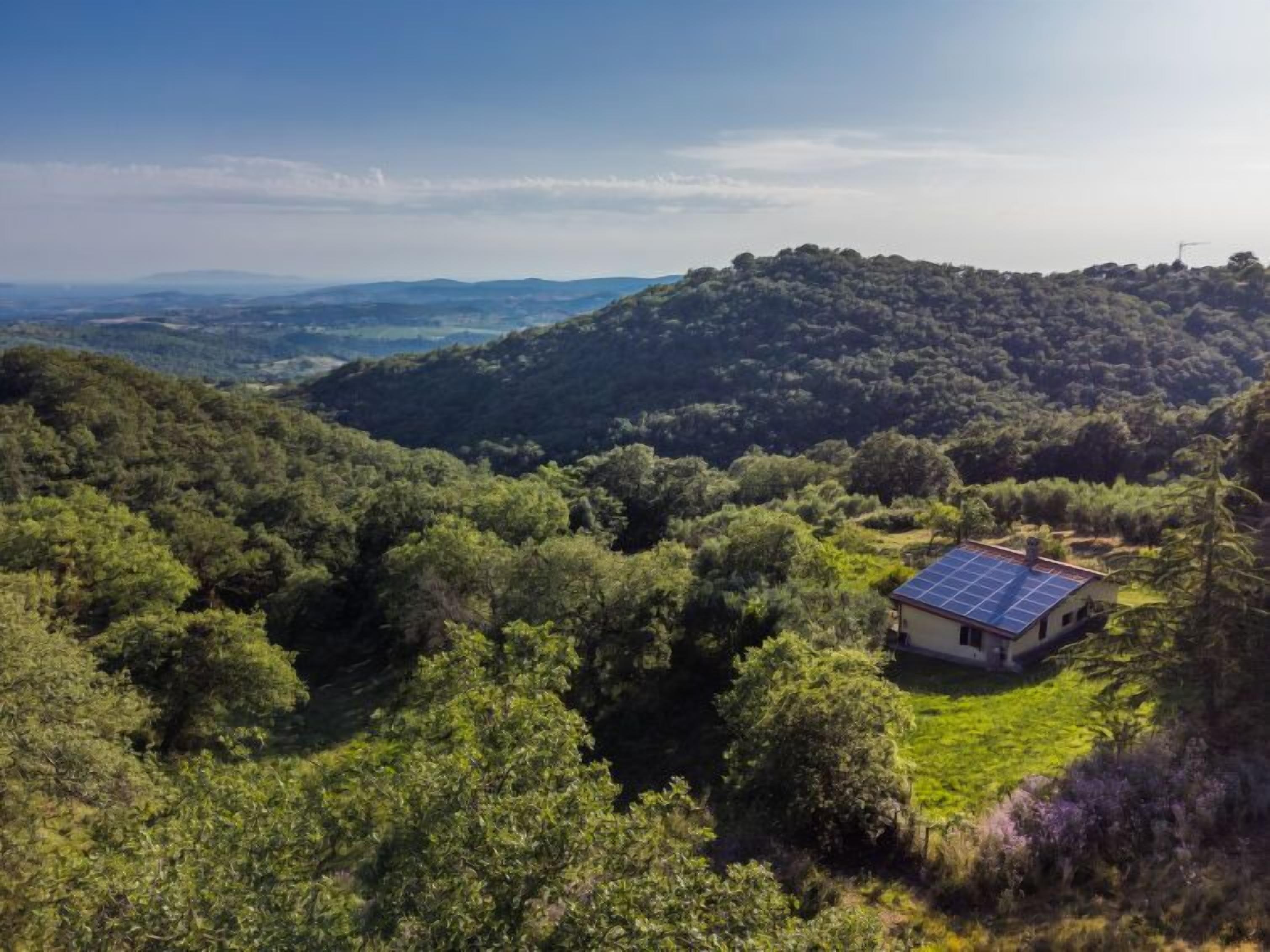 A house with a solar panel roof surrounded by dense forest and hills.