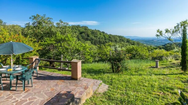 Un pati amb una taula i cadires, un mur de pedra i una vista d'un paisatge verd i exuberant.