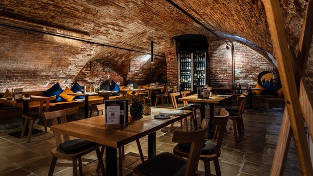 Un intérieur rustique avec des murs en briques, des tables et des chaises en bois, un mur en briques et un luminaire suspendu.