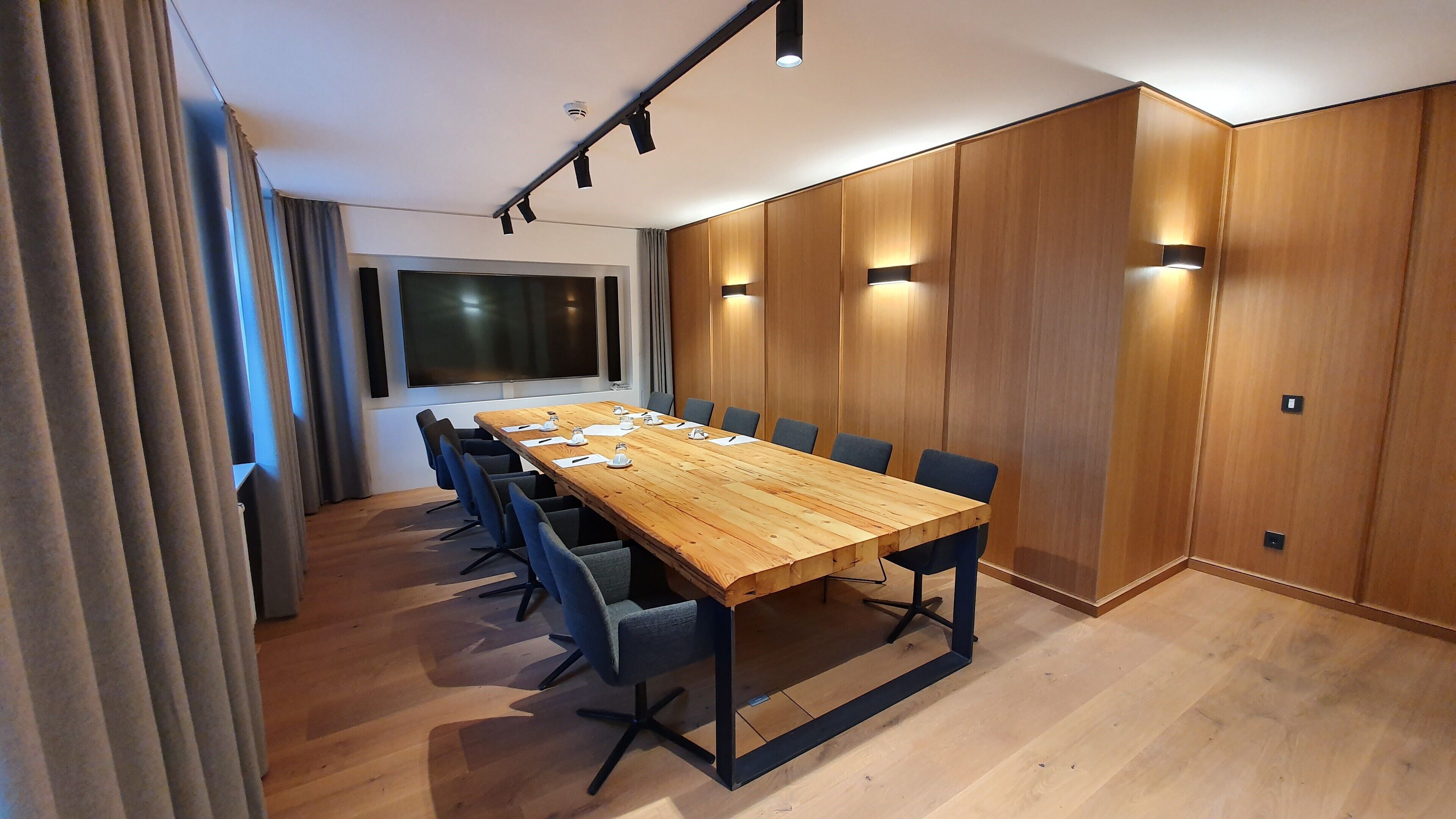 A conference room with a long wooden table, blue chairs, and wooden panel walls.