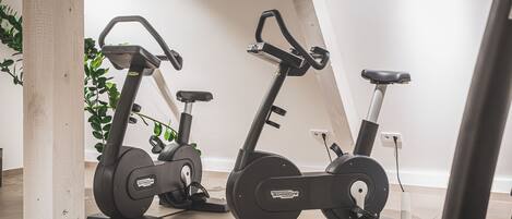 Three stationary bikes in a room with a tiled floor and a plant in the background.