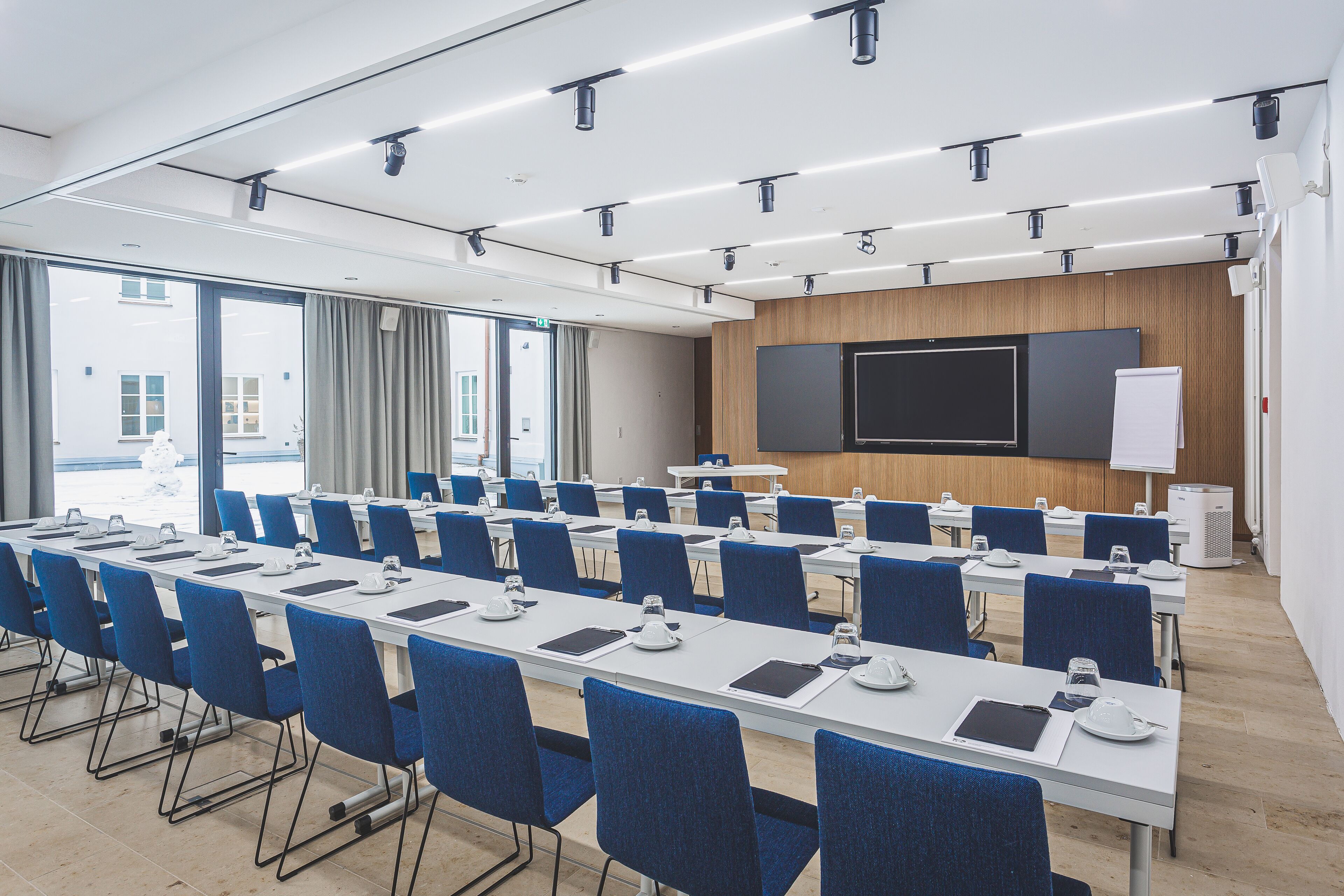 A conference room with long tables, blue chairs, a large screen, and a whiteboard.