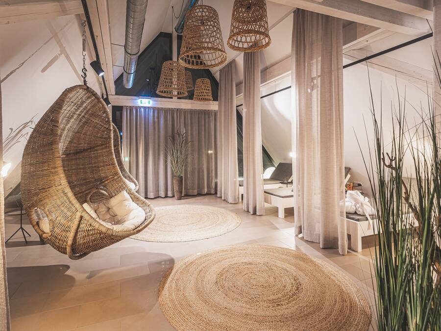 A spacious room with a hanging chair, large woven rugs, and a view of a balcony.