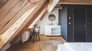 Une chambre de style loft moderne, avec des poutres en bois apparentes, une commode blanche, un miroir rond et une porte sombre.