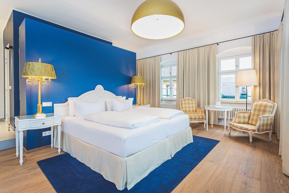 A hotel room with a large bed, two bedside tables, a desk, a chair, and a view of the outside.