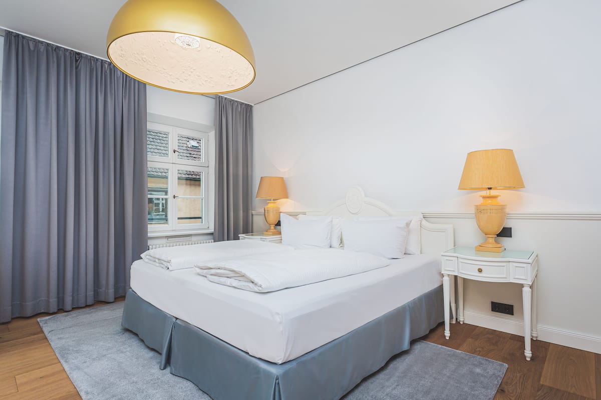 A neatly made bed with white linens, a grey skirt, and two bedside tables with lamps.
