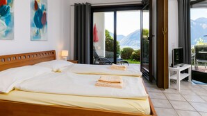 Une chambre d’hôtel avec deux lits, une télévision et un balcon offrant une vue sur la montagne.
